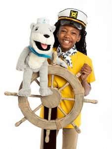 Black preteen girl in captain's hat, holding Oliver T. Otter puppet and one hand on a ship's wheel
