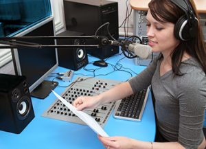 woman wearing headphones and reading into a microphone