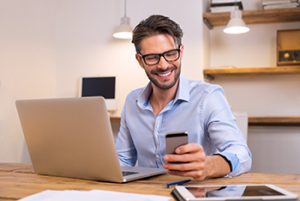 Man wearing glasses smiles at something on phone, perhaps a one-liner